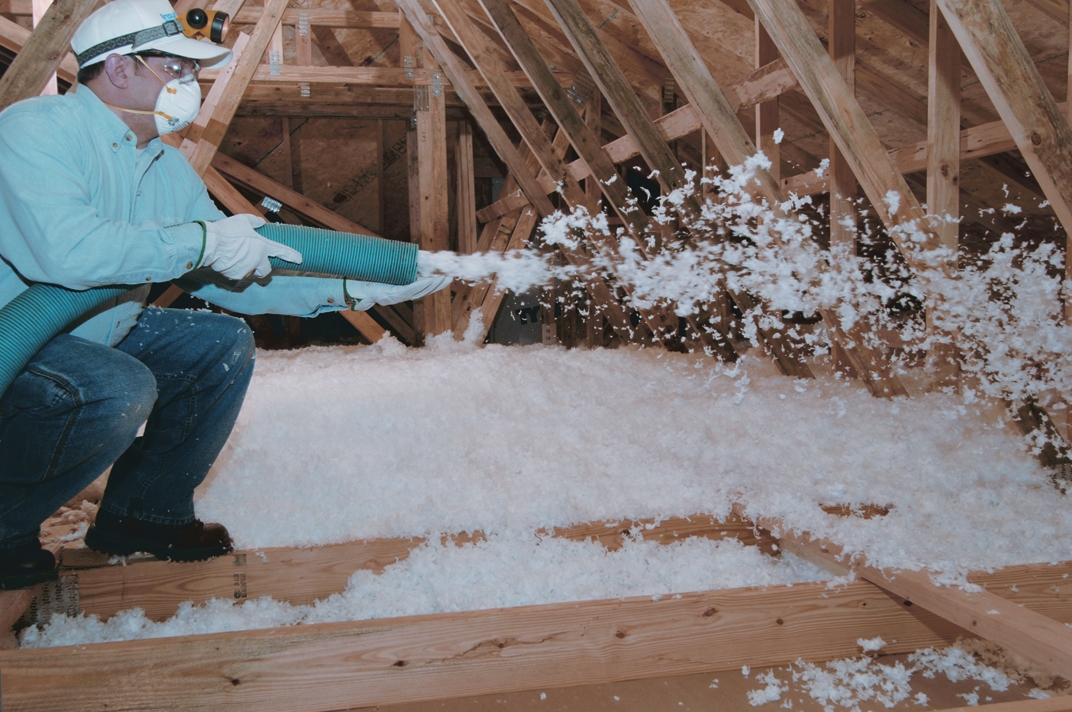 Technician wearing protective gear while filling an attic space with blown-in insulation.